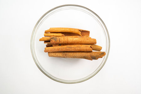 A bowl of cinnamon sticks sits on a white background. The cinnamon sticks are arranged in a way that they are not touching each otherの写真素材