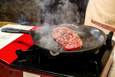 A piece of sirloin meat is cooking in a pan on a stove. The pan is red and black
