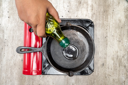 A person is pouring oil into a pan on a stove