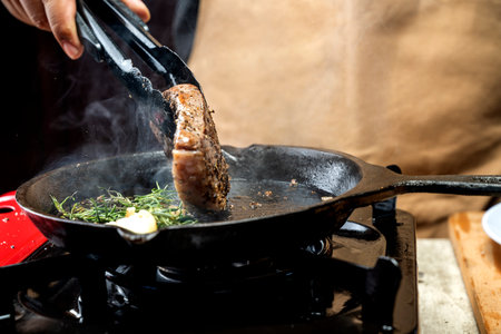 A person is cooking a picanha steak in a pan on a stove
