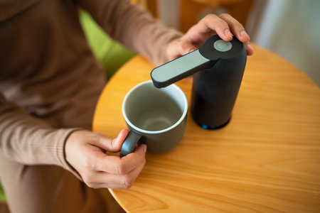 A woman is holding a mug and a device for pouring water from the water gallon. The device is on a...