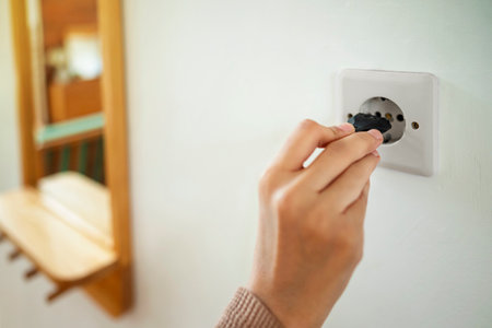 A person is holding a plug in a socket on the wall