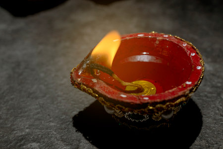 A red and gold decorated pot with a blue and white design sits on a dark surface. A small flame is...