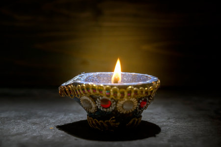 A blue and gold decorated pot with a blue and white design sits on a dark surface. A small flame is burning inside the pot. Diwali conceptの写真素材