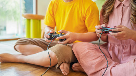 Two people playing a video game together. One of them is wearing a yellow shirt. The girl is wearing...