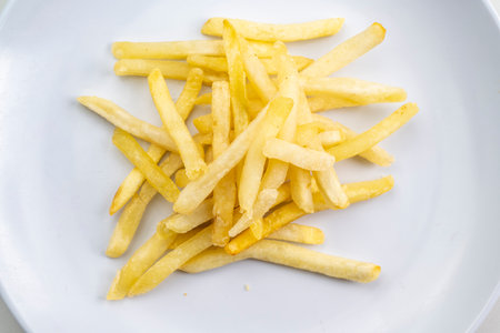 A plate of french fries sits on a white table. The plate is empty and the fries are piled up on top...