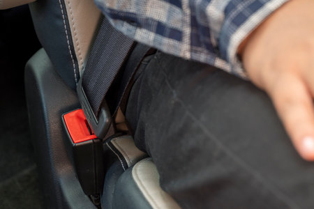 A person is sitting in a car with the seatbelt buckled. The seatbelt is red and blackの写真素材