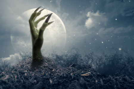 Witch hand with long black nail coming out from grave ground with a full moon in the background. The...