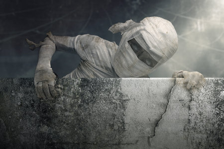Mummy in bandages rising out of behind the wall, with a creepy, dark and scary mood. Ancient...