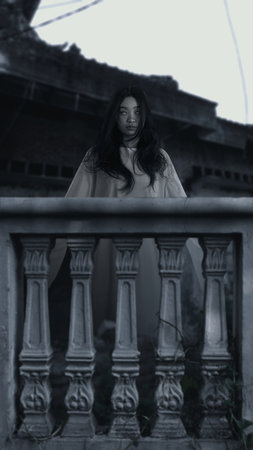 Woman ghost standing behind balustrade. Woman had long hair. The sky is dark and cloudy, and there is a abandoned building in the background. Scene is scary and creepy. Spooky Halloween conceptの写真素材