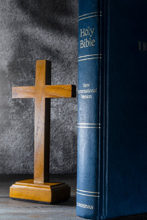 Wooden religion cross and blue book with the word Holy Bible. It is laying on a wooden table. Religious christian holiday. Symbol of faith in God, Christianity Feast. Religious christian conceptの写真素材