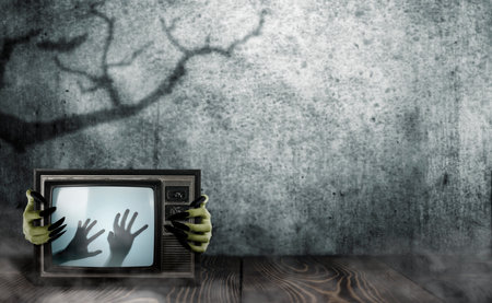 Witch hand with long black nail holding television with shade of zombie hands on screen. The hand...