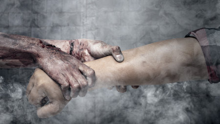 A zombie hand with a bloody wound grabs a human hand in dark room. Scene has dark and scary. Zombie, devil, evil, satan, or monster hands. Spooky Halloween conceptの写真素材