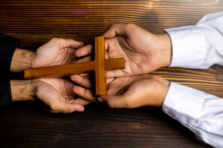 Man holding a religion cross together on wooden background. Symbol of faith and worship in God. People christianity prayer in church. Religious service, holiday or conceptの写真素材