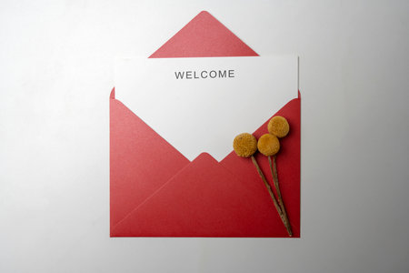 Top view of red envelope and postcard with white card with words Welcome and flowers on it. Welcome greeting for invitation, greet, show acceptance. Design for business or marketing conceptの写真素材