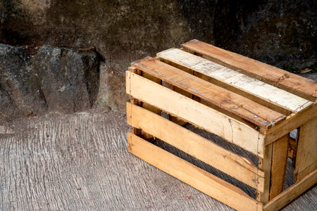 Wooden crate sitting on a concrete floor with stone wall background. Wooden pallet box. The crate is empty and made of wood. Old and wornの写真素材