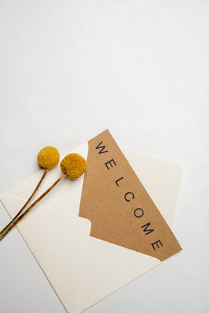 Top view of white envelope and postcard with brown card with words Welcome and flowers on it. Welcome greeting for invitation, greet, show acceptance. Design for business or marketing conceptの写真素材