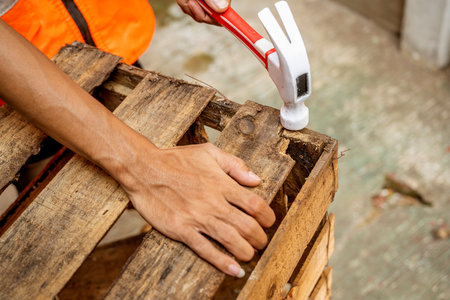 Workers in safety vest using hammer to to work assembling pallet parts. The scene is set in a warehouse background. Woodworking factoryの写真素材