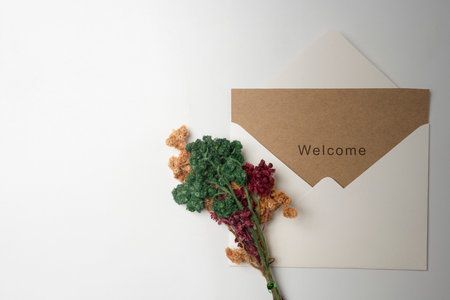 Top view of white envelope and postcard with brown card with words Welcome and flowers on it. Welcome greeting for invitation, greet, show acceptance. Design for business or marketing conceptの写真素材