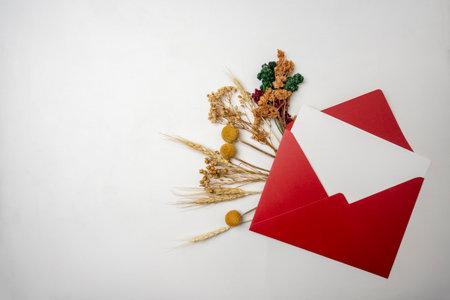 Top view of red envelope and postcard with empty blank white card and flowers on white background. Mockup, copy space. Greeting or invitation card with flat lay styleの写真素材