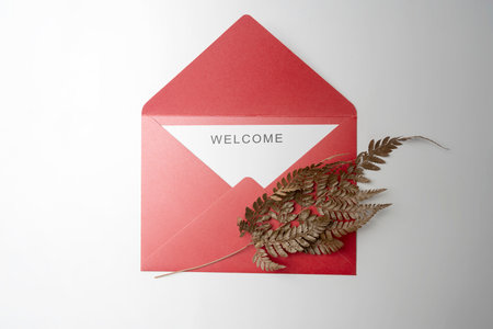 Top view of red envelope and postcard with white card with words Welcome and brown leaves on it. Welcome greeting for invitation, greet, show acceptance. Design for business or marketing conceptの写真素材