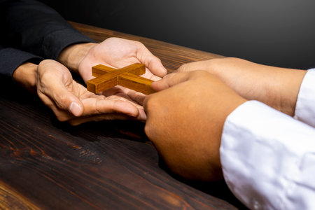 Man giving a religion cross to other on wooden background. Symbol of faith and worship in God. People christianity prayer in church. Religious service, holiday or conceptの写真素材