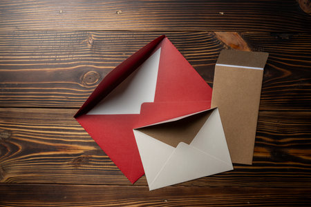 Top view of stack of three envelope and postcard on wooden background. The envelopes are of different variation size and colors. Mockup, blank template, copy space. Greeting or invitation card with flat lay styleの写真素材