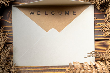 Top view of envelope and postcard with brown card with words Welcome on it and wreath. Greeting for invitation, express hospitality, greet, show acceptance. Design for business or marketing conceptの写真素材