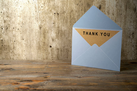 White envelope and postcard with brown card with words Thank You written on it on the table. Thank...