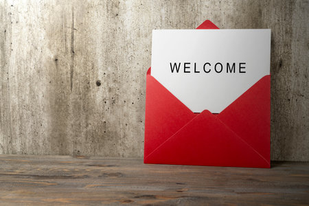 Red envelope and postcard with white card with words Welcome on it on the table. Greeting for invitation, express hospitality, greet, show acceptance. Design for business or marketing conceptの写真素材