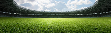 Empty football stadium with green field and blue sky. The field is ready for a game. Concept of Professional sport, Competition, Championship and match. Soccer stadium field backgroundの写真素材