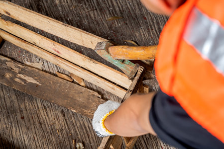Workers in safety vest and glove using axe to work disassembling pallet parts. The scene is set in a warehouse background. Woodworking factoryの写真素材