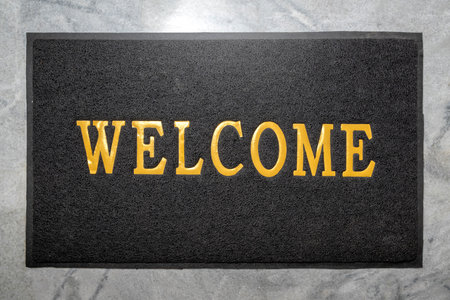 Top view of black doormat with welcome text on it with floor background. Welcome greetings sign....