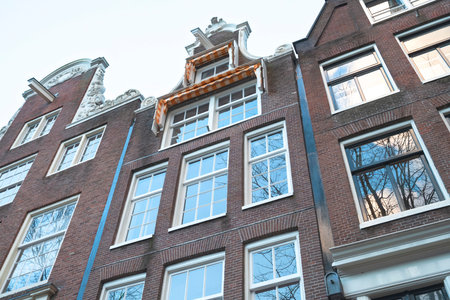 Low angle view of several tall buildings in a row with old style and have many windows of geometric shapes with clear sky background in Amsterdam, Netherlandsの写真素材