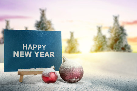 Closeup view of Christmas balls with the text of Happy New Year on an envelope on a wooden easel with a snowfield background. Decoration for New Year celebrationの写真素材