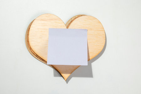 Wooden heart with empty white paper on a white background. Copy space. Mockup. Valentine Card. Decoration for Valentine celebrationの写真素材