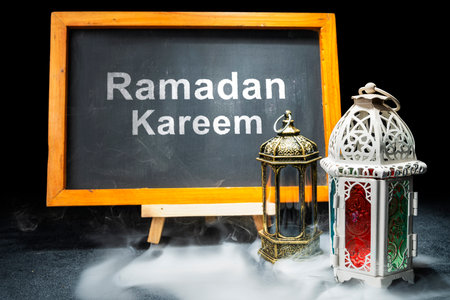 Wooden easel and chalkboard with the text of Ramadan Kareem and Arabic lanterns on a black background. Decoration for Muslim holidays celebrationの写真素材