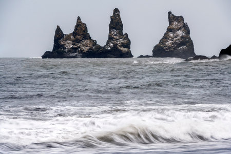 Panoramic view of ocean waves with protruding rocks from black sand beach Reynisfjara, Iceland....