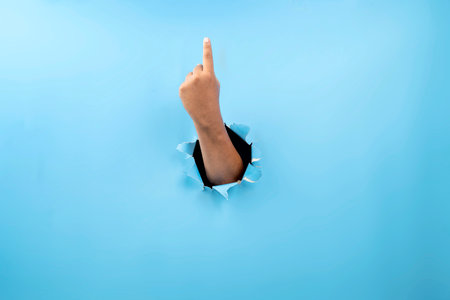 Human hand showing from ripped paper. Hand gestures of pointing up. Mockup or Copy space. Concept of sign or communicationの写真素材