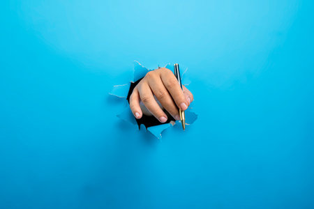 Human hand holding ballpoint pen through ripped paper. Mockup or Copy space. Concept of business, signature, communication, or handwritingの写真素材