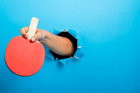 Human hand holding table tennis paddle through ripped paper. Mockup or Copy space. Concept of sportの写真素材