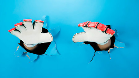 Human hand wearing goalkeeper gloves through ripped paper. Mockup or Copy space. Concept of sportの写真素材