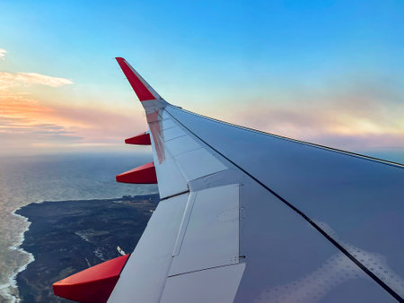 View the airplane wing in clouds with an ocean and land during a flight in the sky. Nature, horizon, travel background, or wallpaperの写真素材