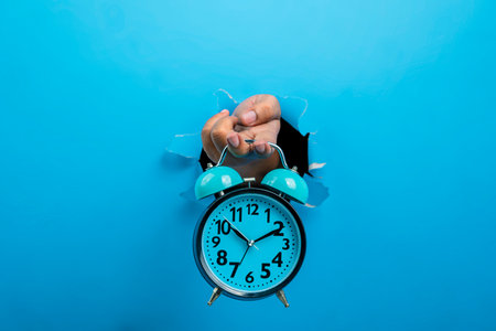 Human hand holding alarm clock through ripped paper. Mockup or Copy space. Concept of time...