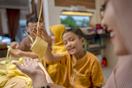 Indonesian Muslim family weaving ketupat rice dumpling from young coconut leaves. Traditional Muslim food during celebration of Happy Lebaran, Eid Al Fitr, Idul Fitri, and Ramadan Mubarak celebrationの写真素材