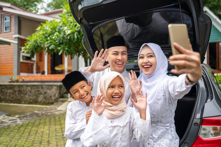 Indonesian Muslim family with mobile phone take selfie or video call before mudik or traveling to their hometown. Concept of Happy Lebaran, Eid Al Fitr, Idul Fitri, and Ramadan Mubarak celebrationの写真素材