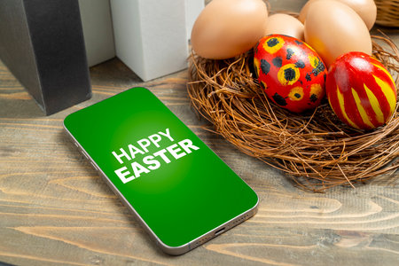 The nest filled with colorful decorated easter eggs and happy easter greetings on the mobile phone screen. Concept of celebrating the easter holidayの写真素材