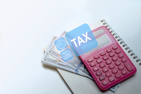Pink calculator and a pile of 100 dollar banknotes on a notebook with a white background. Concept of finance and taxationの写真素材