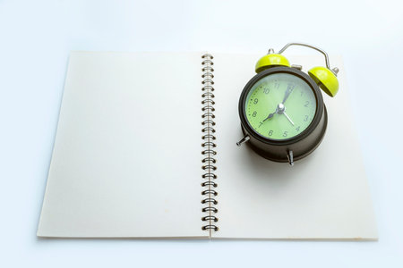 Green alarm clock and notebook on white background. Empty area for mockup or copy space. Concept of study or educationの写真素材