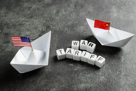 Paper boat with the USA and China flags with cubes with the text of war tariff on a black background. Concept of the United States of America versus China trade war disputes or economic conflictの写真素材